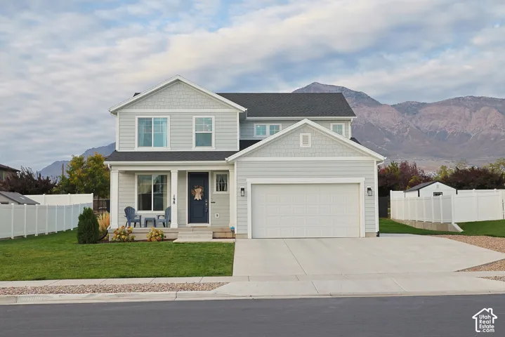 Two-story residence featuring light-toned horizontal lap siding, shake shingle gables, a covered front porch, and a concrete driveway leading to an attached two-car garage