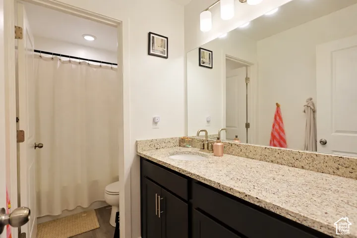 Dark cabinetry vanity featuring a stone-composite countertop, undermount sink, brushed nickel faucet, large wall-mounted mirror, and multi-bulb vanity light fixture