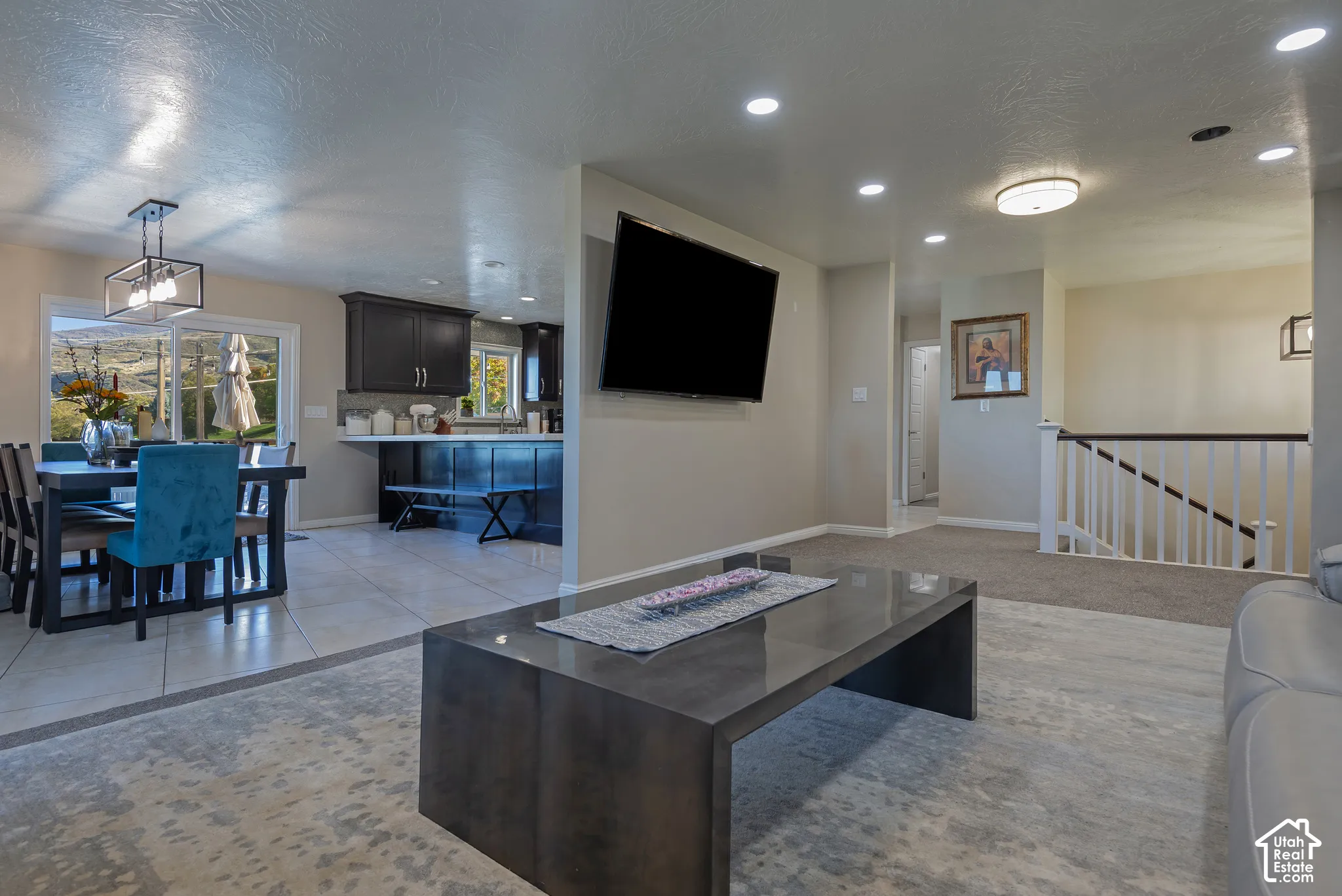 Open-concept main level featuring dark cabinetry, ceramic tile flooring, recessed lighting, and a white baluster staircase