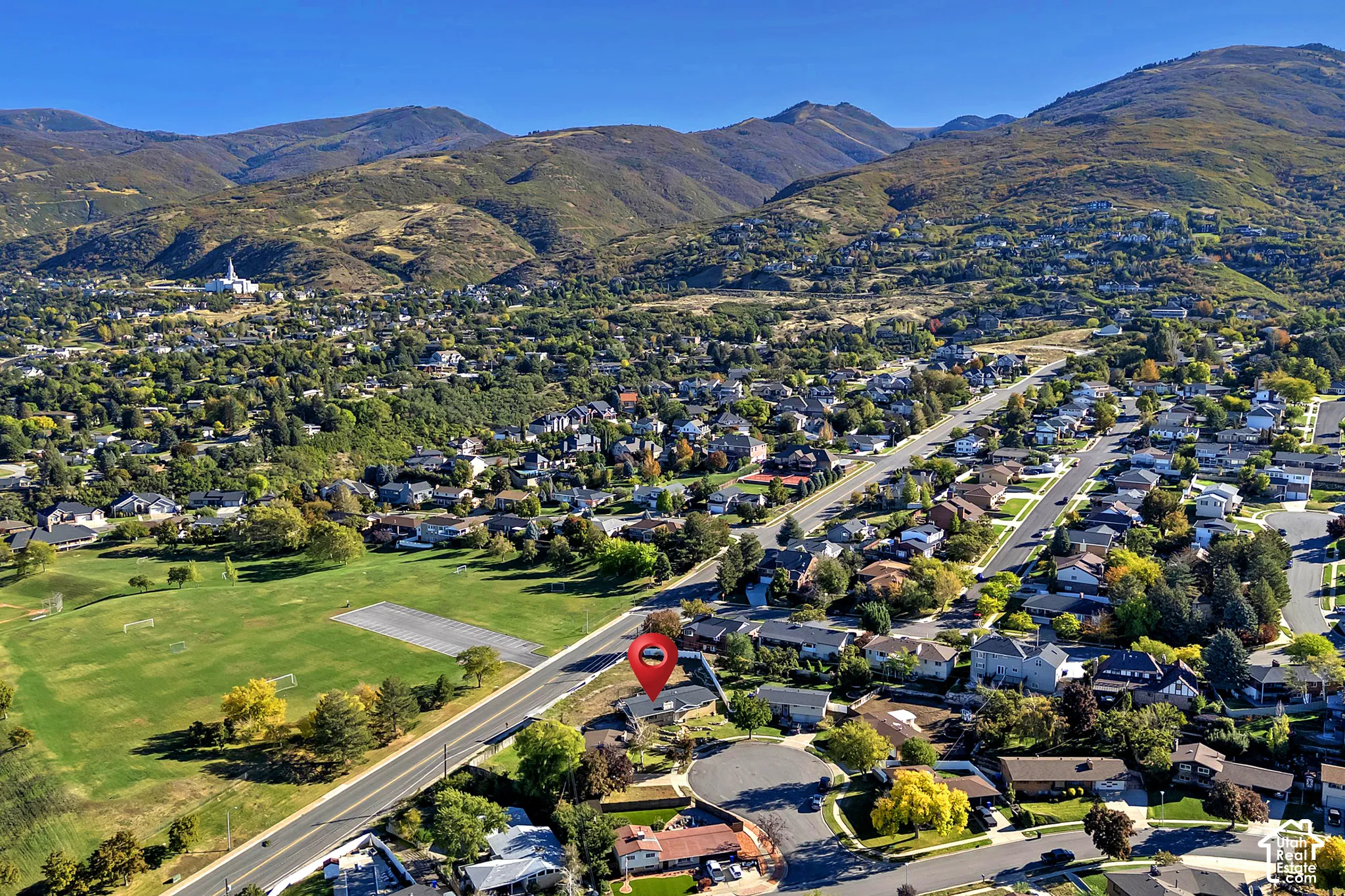 Aerial perspective of a residential property featuring a mountain backdrop, mature trees, and proximity to expansive green space