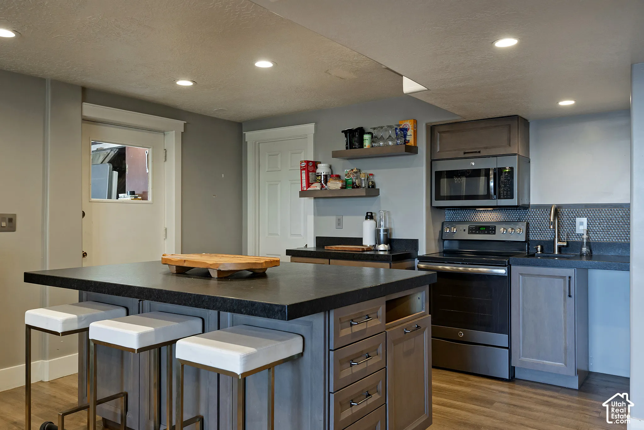 Kitchen featuring a central island with a solid surface countertop, dark-toned cabinetry, recessed lighting, wood-finish flooring, and a hexagonal tile backsplash