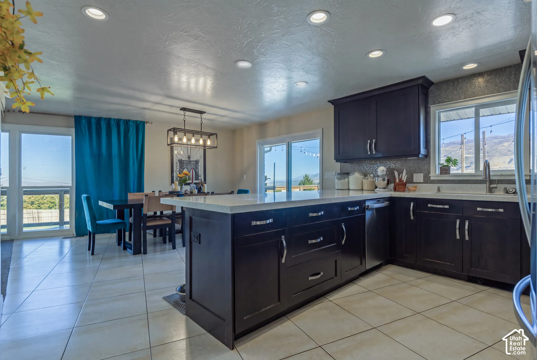 Kitchen featuring dark wood cabinetry, light stone countertops, ceramic tile flooring, recessed lighting, and a multi-light pendant fixture