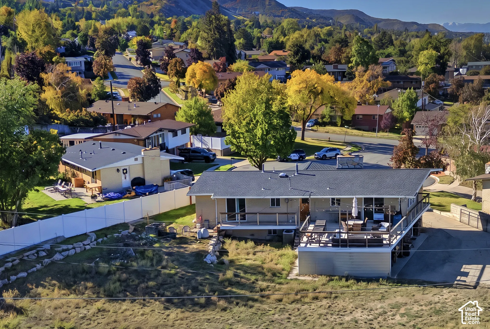 Exterior featuring an elevated wood-railing deck, hardscaped patio area, perimeter vinyl fencing, and mountain backdrop