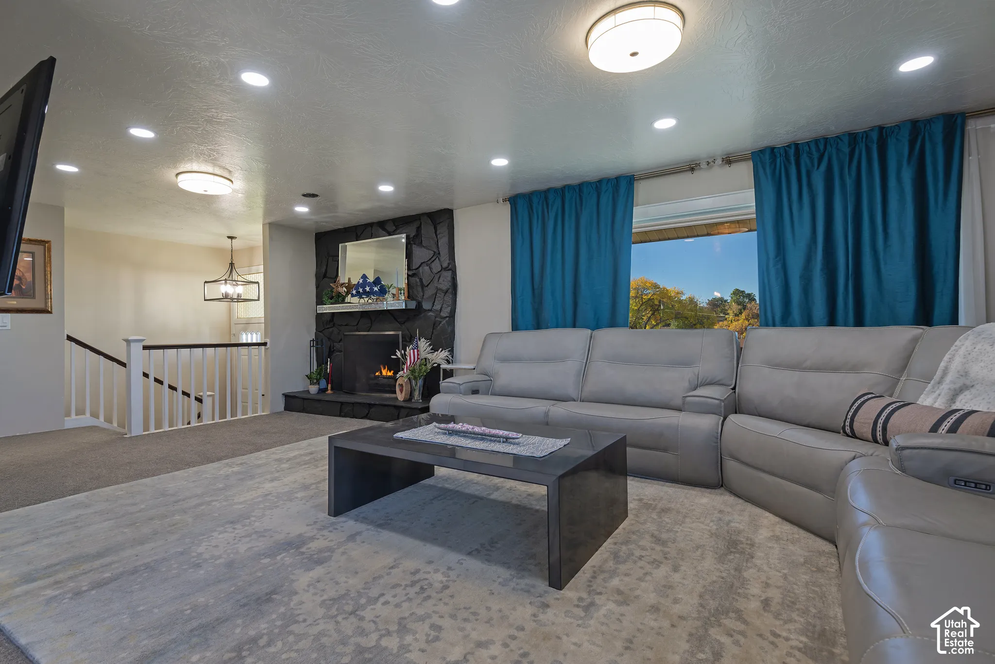 Living area featuring a floor-to-ceiling stone fireplace, recessed lighting, carpeted flooring, and a staircase with white balusters