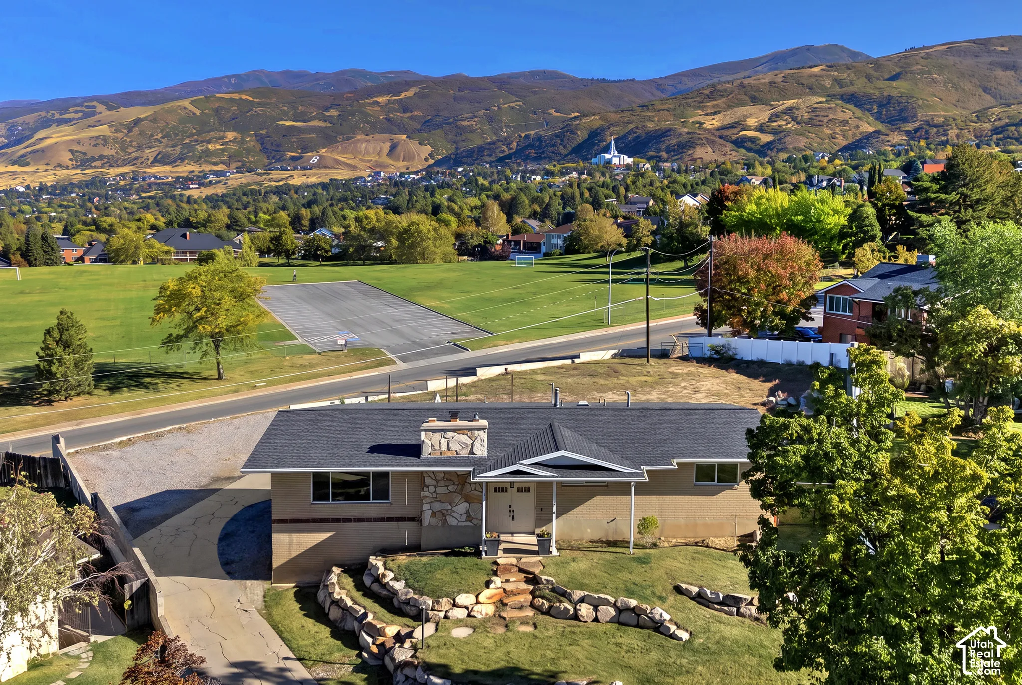 Single-story residence featuring a stone masonry chimney, terraced stone retaining walls, and a multi-pitched roofline, set against a backdrop of mountain scenery