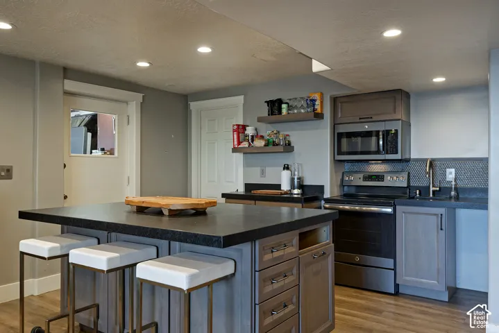 Kitchen featuring a central island with a solid surface countertop, dark-toned cabinetry, recessed lighting, wood-finish flooring, and a hexagonal tile backsplash