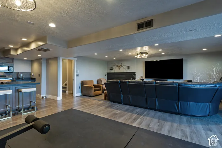 Open-concept area featuring recessed lighting, wood-finish flooring, a wet bar with stone-surfaced countertops, and a fireplace with a decorative mantel