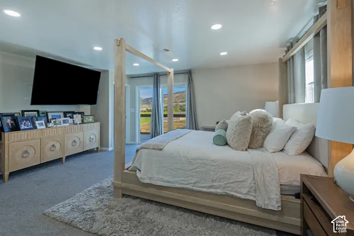 Recessed ceiling lighting, wall-mounted television, and sliding glass doors leading to an exterior balcony with mountain scenery