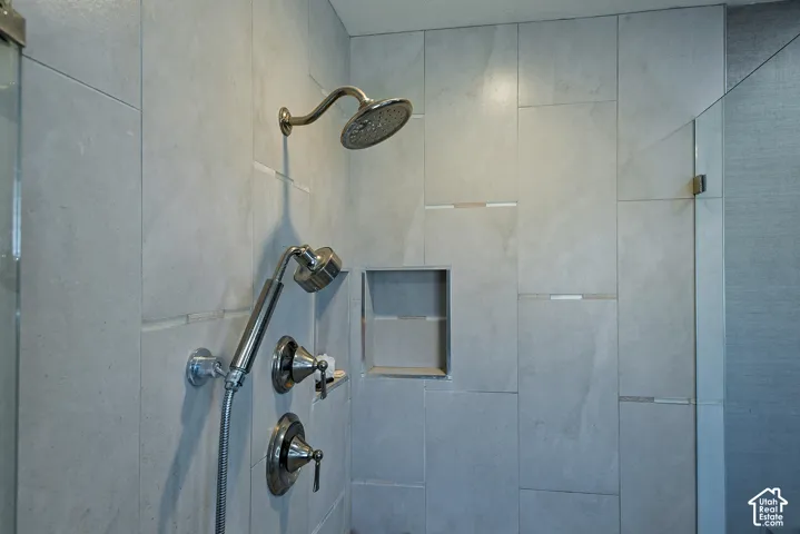 Shower enclosure featuring large-format ceramic tile, a wall-mounted shower head, a handheld sprayer, metal hardware, and a built-in recessed wall niche