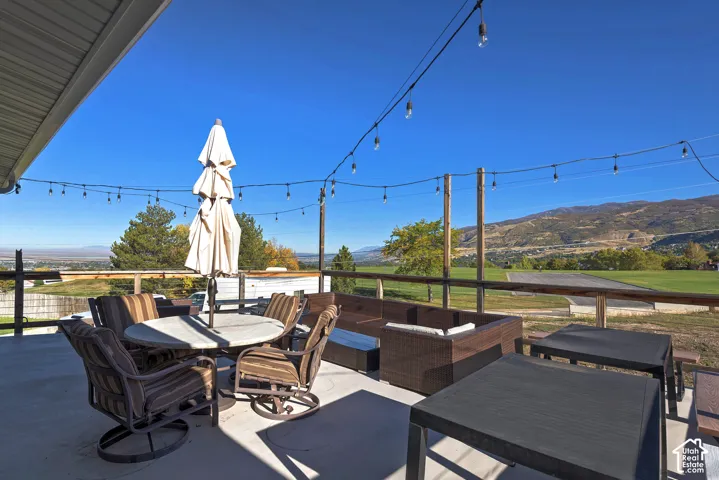 Elevated concrete patio featuring a wooden railing, overhead string lighting, and mountain terrain backdrop
