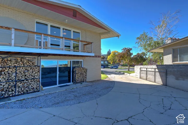 Exterior featuring a brick facade, upper-level deck with a wood railing, sliding glass doors, and a concrete driveway