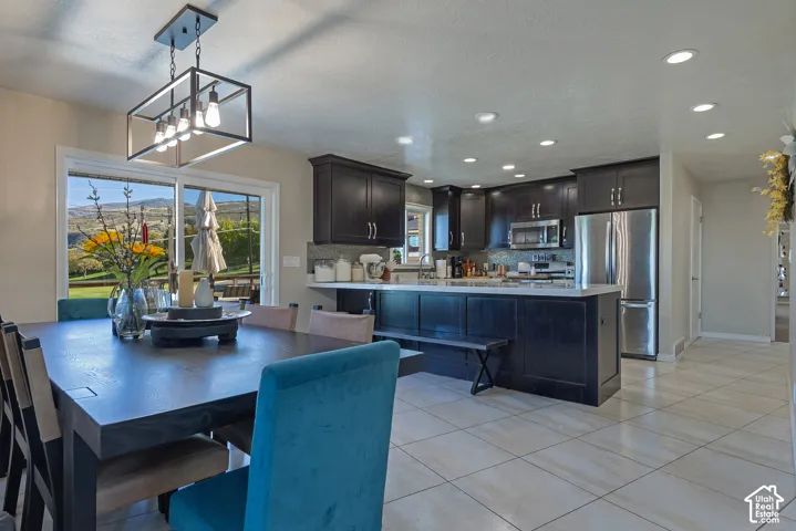 Kitchen featuring dark-finish cabinetry, quartz countertops, stainless steel appliances, tile flooring, and a linear pendant light fixture
