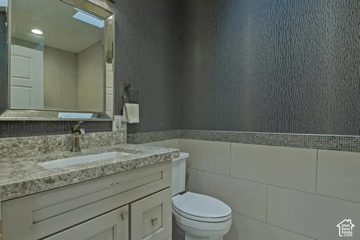 Vanity with stone-finish countertop and integrated sink, framed wall mirror, textured wallpaper, mosaic tile accent border, and large-format wall tiling