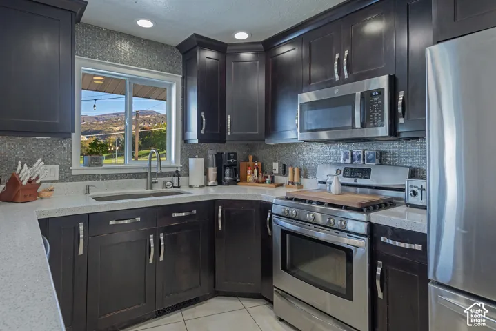 Dark wood cabinetry paired with quartz countertops, stainless steel appliances, a tile backsplash, and ceramic tile flooring