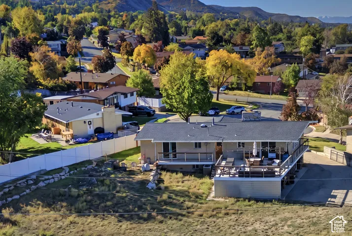 Exterior featuring an elevated wood-railing deck, hardscaped patio area, perimeter vinyl fencing, and mountain backdrop