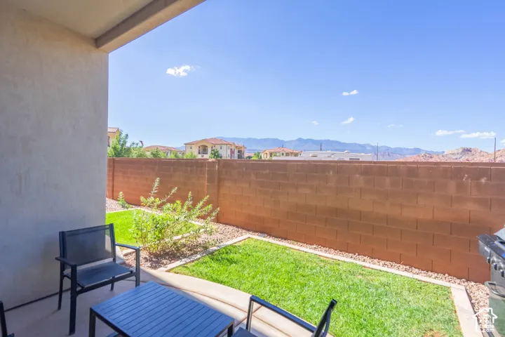 Covered concrete patio featuring a landscaped lawn, desert stone borders, and a masonry privacy wall against a mountain backdrop