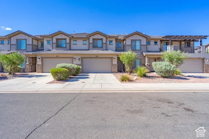 Multi-unit residence featuring neutral stucco siding, stone veneer accents, multi-car garages, and a second-story balcony with a wooden pergola