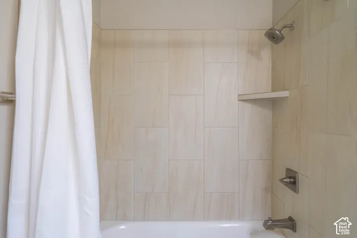 Shower enclosure featuring large-format neutral-toned wall tile, a built-in corner shelf, and metallic fixtures including a fixed shower head and single-handle mixing valve