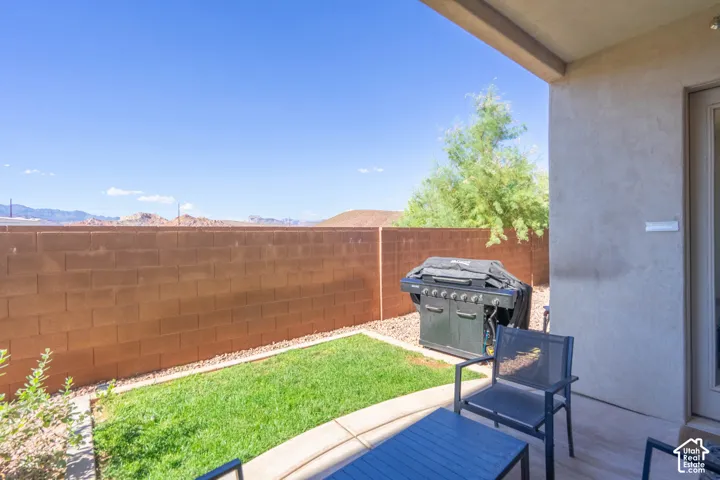 Covered patio featuring concrete flooring, a fenced backyard with a grass lawn, and a backdrop of mountain scenery