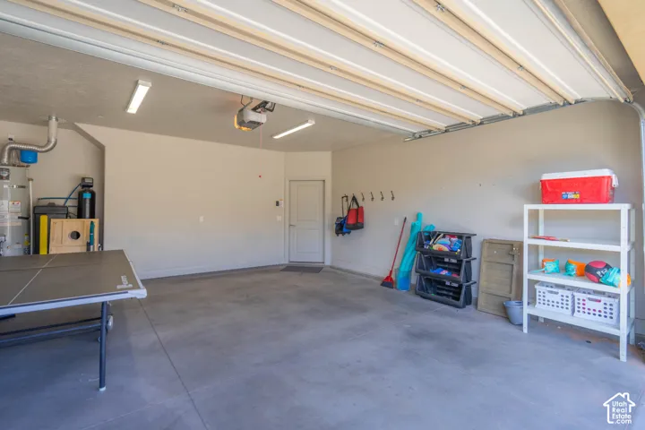 Finished garage interior featuring concrete flooring, an automated overhead door, dual linear lighting fixtures, and a side-entry door