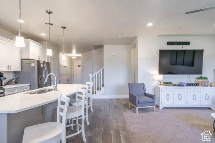 Kitchen featuring a central island with a solid surface countertop, stainless steel refrigerator, white shaker-style cabinetry, and recessed lighting combined with three pendant lights