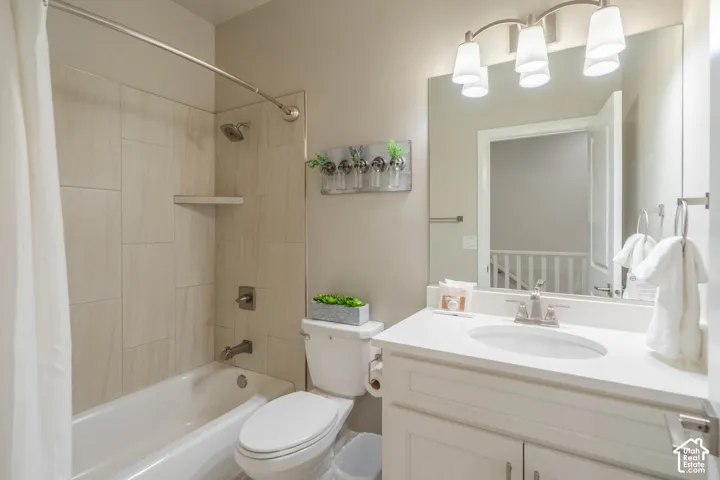 Full bathroom featuring a white vanity with a solid surface countertop and integrated oval sink, large wall-mounted mirror, three-bulb vanity light fixture, and tile-surround shower and tub combination