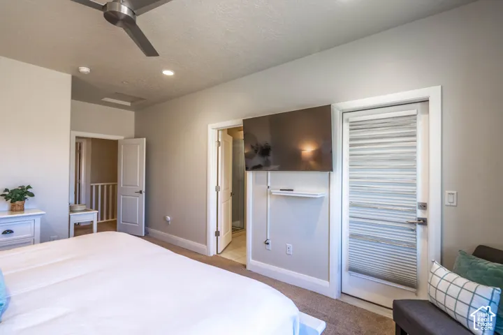 Neutral-toned bedroom featuring a ceiling fan, plush carpeting, multiple interior doors, and a glass-paneled exterior door with integrated blinds