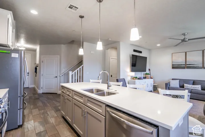 Kitchen island with dual-basin stainless steel sink and white solid-surface countertop, cabinetry with metallic hardware, wood-finish flooring, and pendant lighting