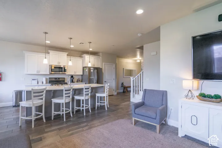 Kitchen featuring white shaker-style cabinetry, quartz-style countertops, stainless steel appliances, a center island with pendant lighting, and wood-finish tile flooring
