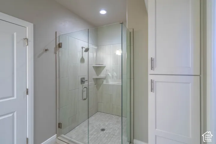 Walk-in shower featuring a frameless glass enclosure, floor-to-ceiling tile surround, built-in shelving, and white shaker-style cabinetry with satin nickel hardware