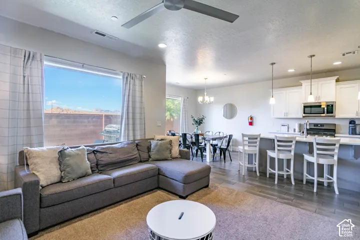 Open-concept interior featuring wood-finish flooring, a kitchen island with pendant lighting, white cabinetry, recessed lighting, and a ceiling fan