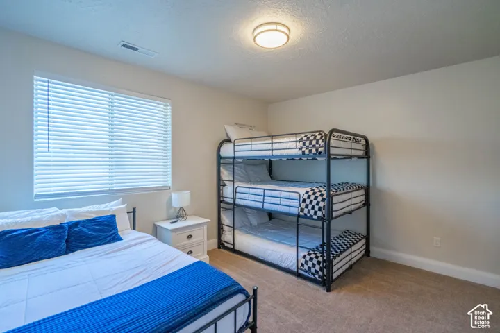 Neutral-toned bedroom featuring carpeting, a single window with horizontal blinds, and a circular flush-mount ceiling fixture