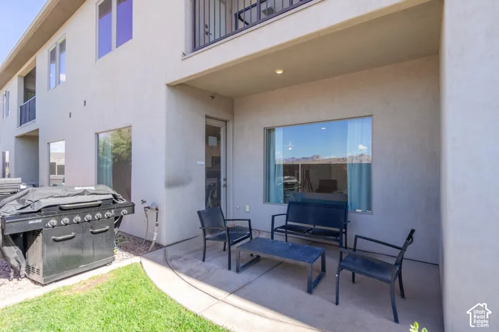 Covered concrete patio featuring a stucco exterior, large windows, and a second-story metal balcony
