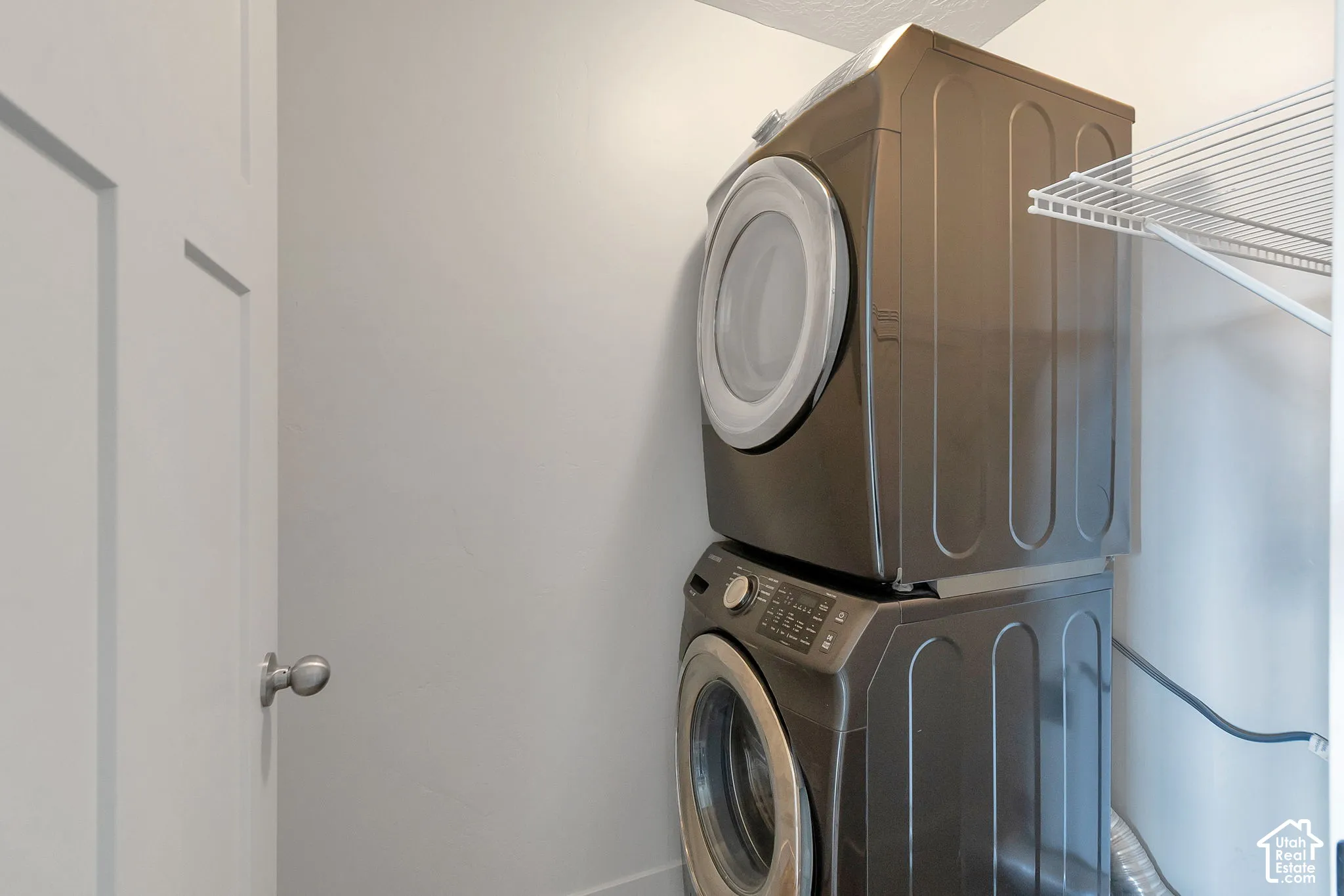 Laundry closet featuring a metallic-finish stacked front-load washer and dryer set and a white wire shelf