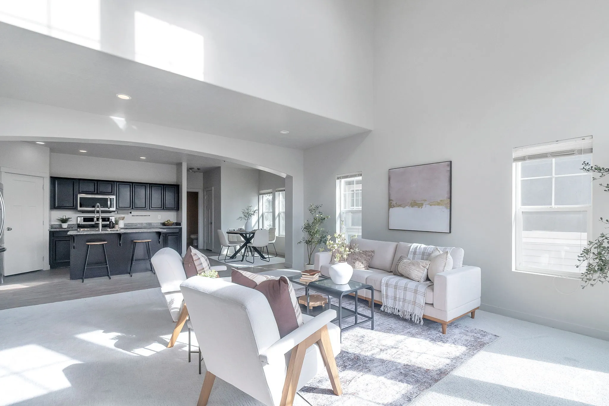 High-ceilinged interior featuring a kitchen with dark cabinetry, breakfast bar, recessed lighting, and large windows