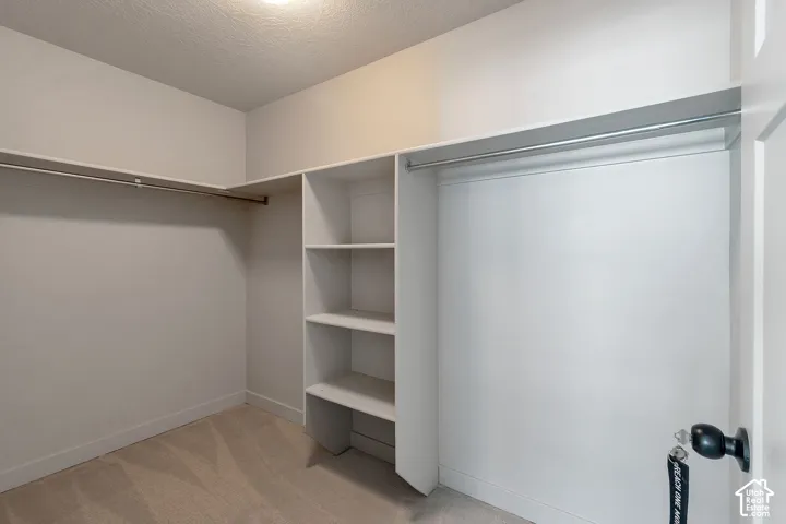 Walk-in closet featuring white built-in shelving, dual metal clothing rods, and wall-to-wall carpeting