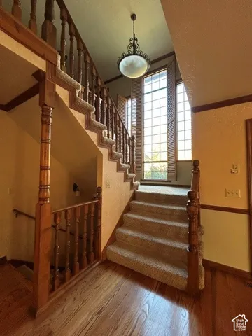 Staircase featuring wood railings and newel posts, carpeted treads, floor-to-ceiling multi-pane windows, and a decorative pendant light fixture