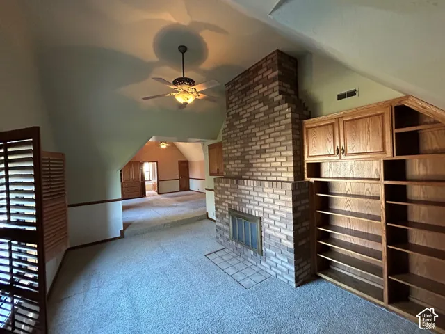 Upstairs Master Bedroom's sitting room-Vaulted ceiling with a central paddle fan, full-height masonry fireplace, and custom built-in wood shelving units with integrated cabinetry
