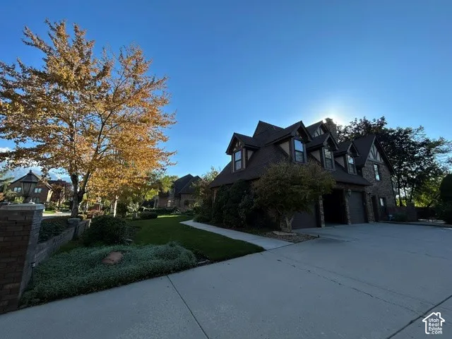 Corner View of Property - southwesterly. Exterior facade featuring multi-gabled rooflines, stone and brick construction, multi-car garage, and landscaped grounds with mature trees