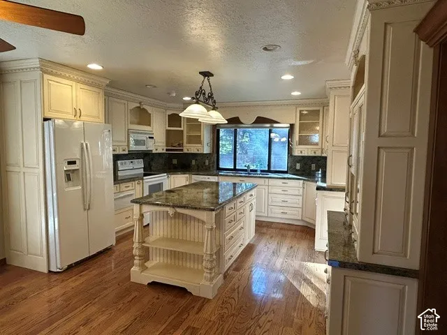 Kitchen featuring custom off-white cabinetry, stone-surfaced countertops, a center island with integrated shelving, wood-finish flooring, and recessed lighting