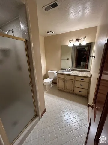 Downstairs Bathroom featuring a vanity with stone-finish countertop, undermount sink, multi-drawer cabinetry, large wall-mounted mirror with decorative light fixture, and walk-in shower with frosted glass enclosure