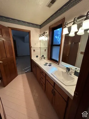 Upstairs bathroom 2 Dual-sink vanity with tile countertop, integrated basin sinks, wooden cabinetry, multi-light wall fixtures, and tiled flooring