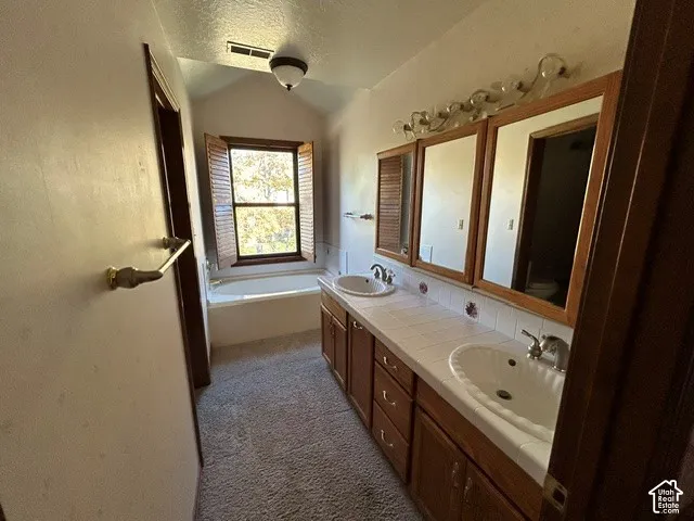 Upstairs Master Bathroom Dual-sink vanity with tile countertop, integrated medicine cabinets, soaking tub, and operable wooden window shutters