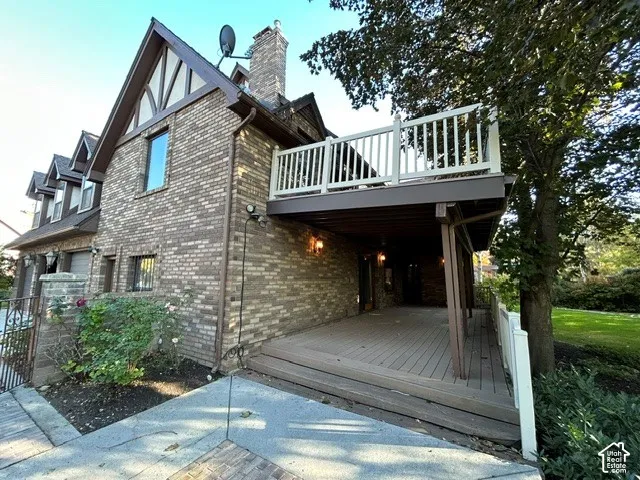 Multi-level home exterior featuring classic brick masonry, half-timbering accents, a stacked stone chimney, and an elevated composite back deck with white railings over a covered patio