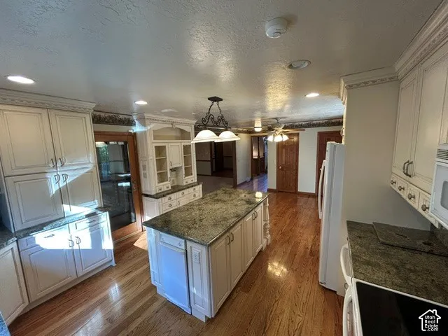 Kitchen featuring off-white cabinetry with crown molding, stone-finish countertops, central island, wood-finish flooring, and recessed lighting