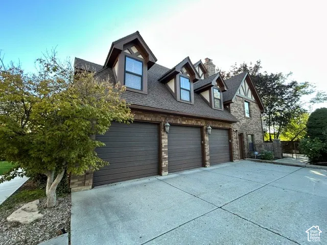 Tudor-style exterior featuring a stone and brick facade, a three-car garage, three dormer windows, and detailed timber framing