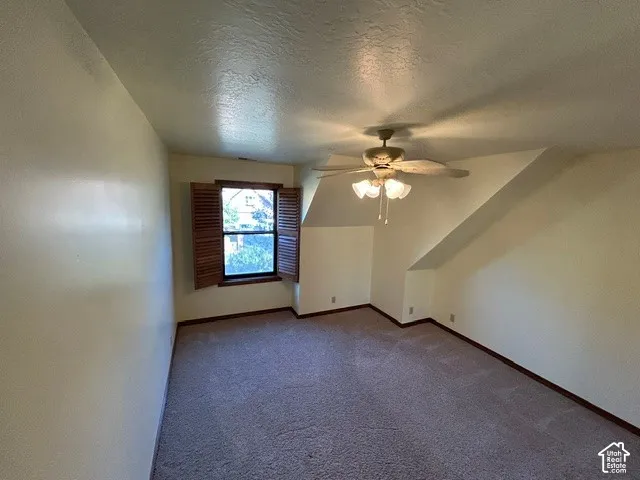 Upstairs Bedroom one featuring slanted ceiling architecture, wall-to-wall carpeting, window with hinged wooden shutters, and a central ceiling fan with integrated light fixture