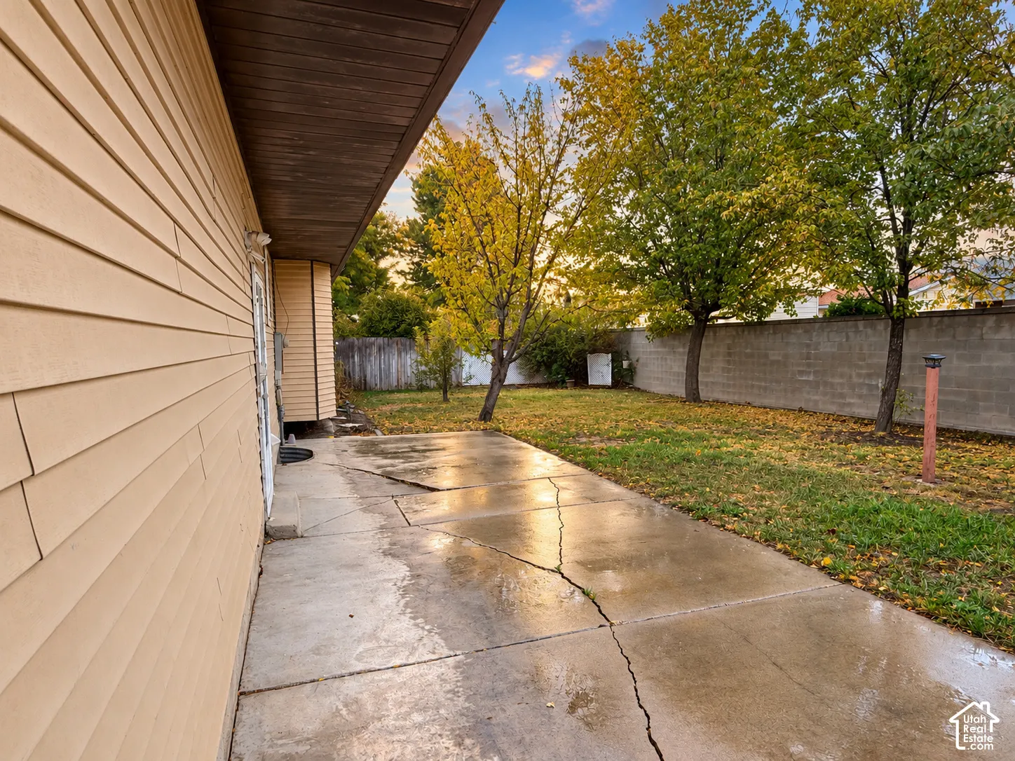 Concrete patio featuring horizontal siding, mature trees, and a concrete block perimeter wall