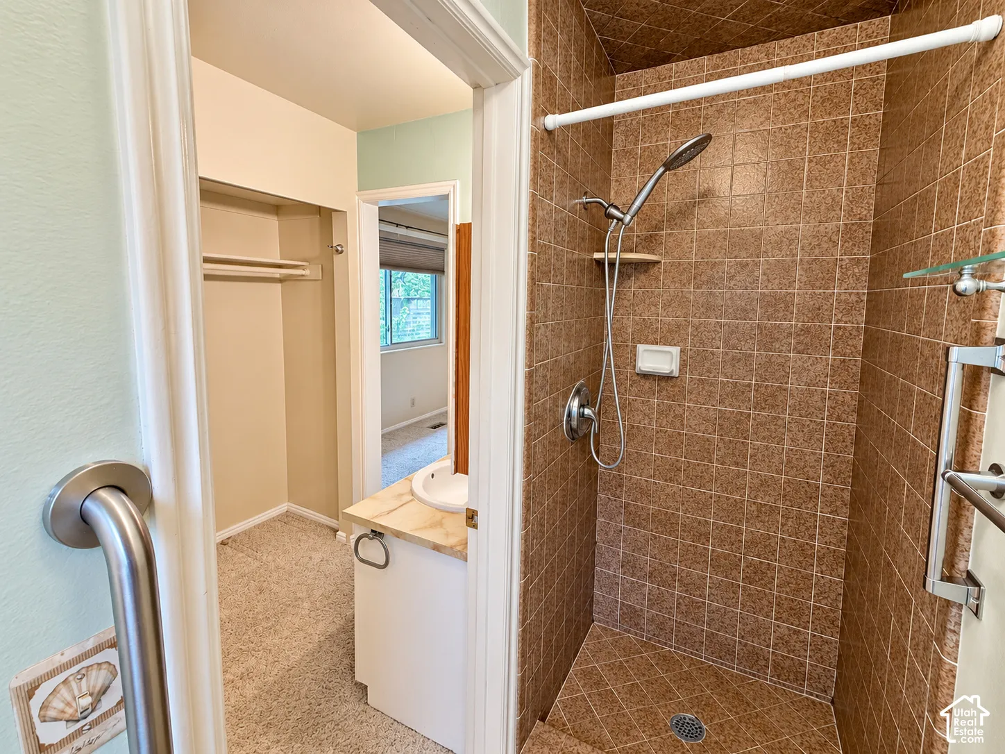 Walk-in shower featuring textured ceramic tile surround, integrated shower shelving, and an adjustable handheld showerhead
