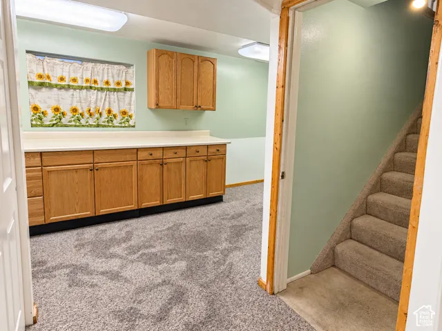 Wood-finish cabinetry with extensive counter space, solid-surface countertops, and carpeted flooring throughout